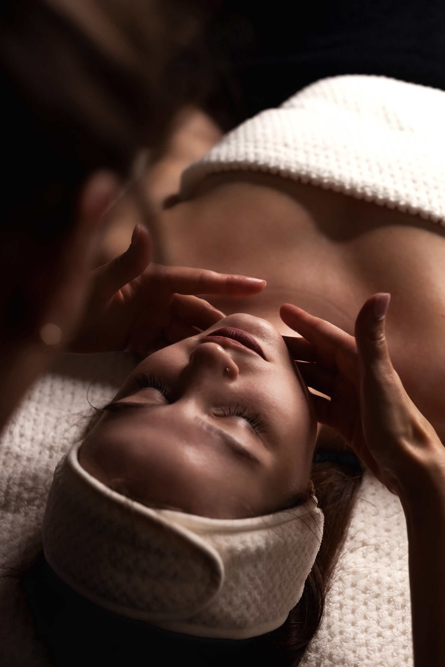 Masseur woman making relax facial massage for beauty lady in medical spa room in shadow